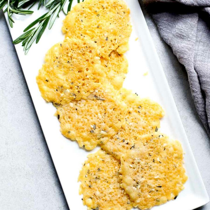 Rosemary Parmesan Cheese Crisps on a white plate with a sprig of rosemary