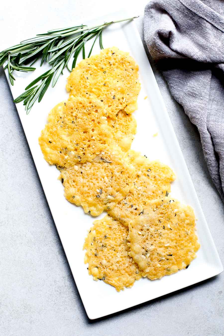 Rosemary Parmesan Cheese Crisps on a white plate with a sprig of rosemary