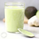 Creamy Avocado Lime Dressing in a jar with avocado and garlic in background