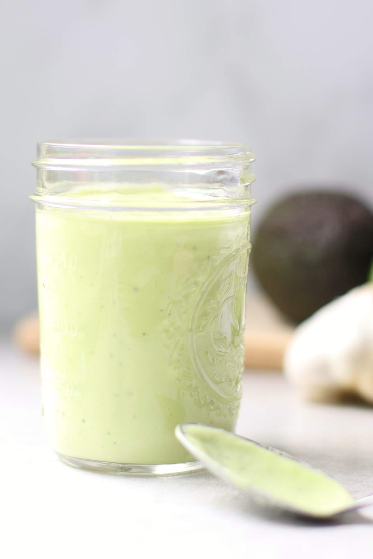 Avocado Lime Dressing in a jar with avocado and garlic in background