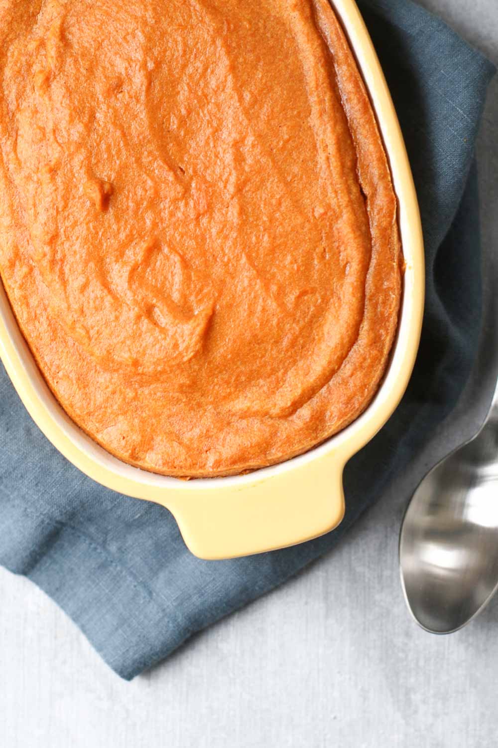 Baked Sweet Potato Pudding in a yellow baking dish with a spoon
