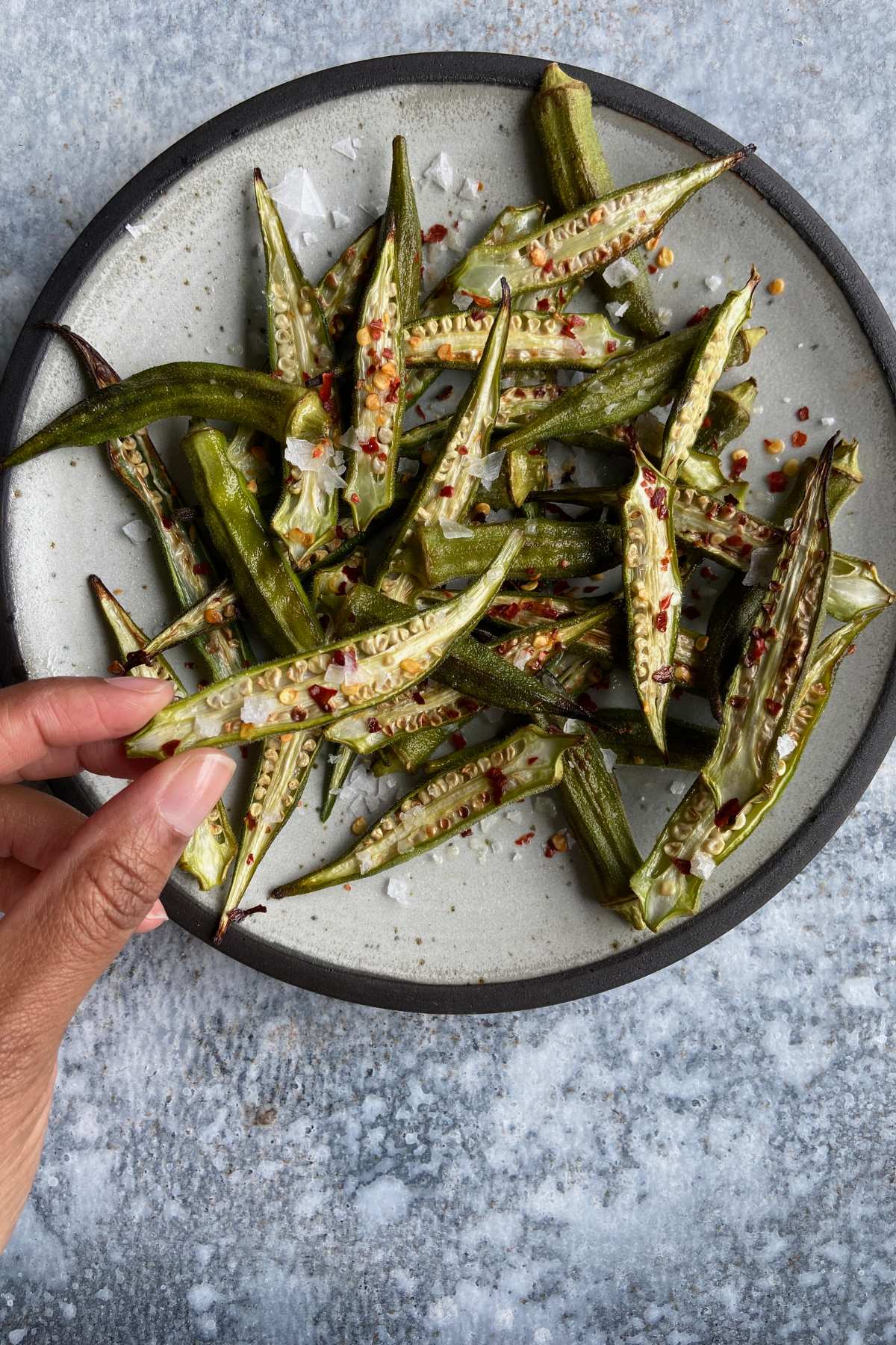 Roasted okra on a plate with Marisa holding one piece