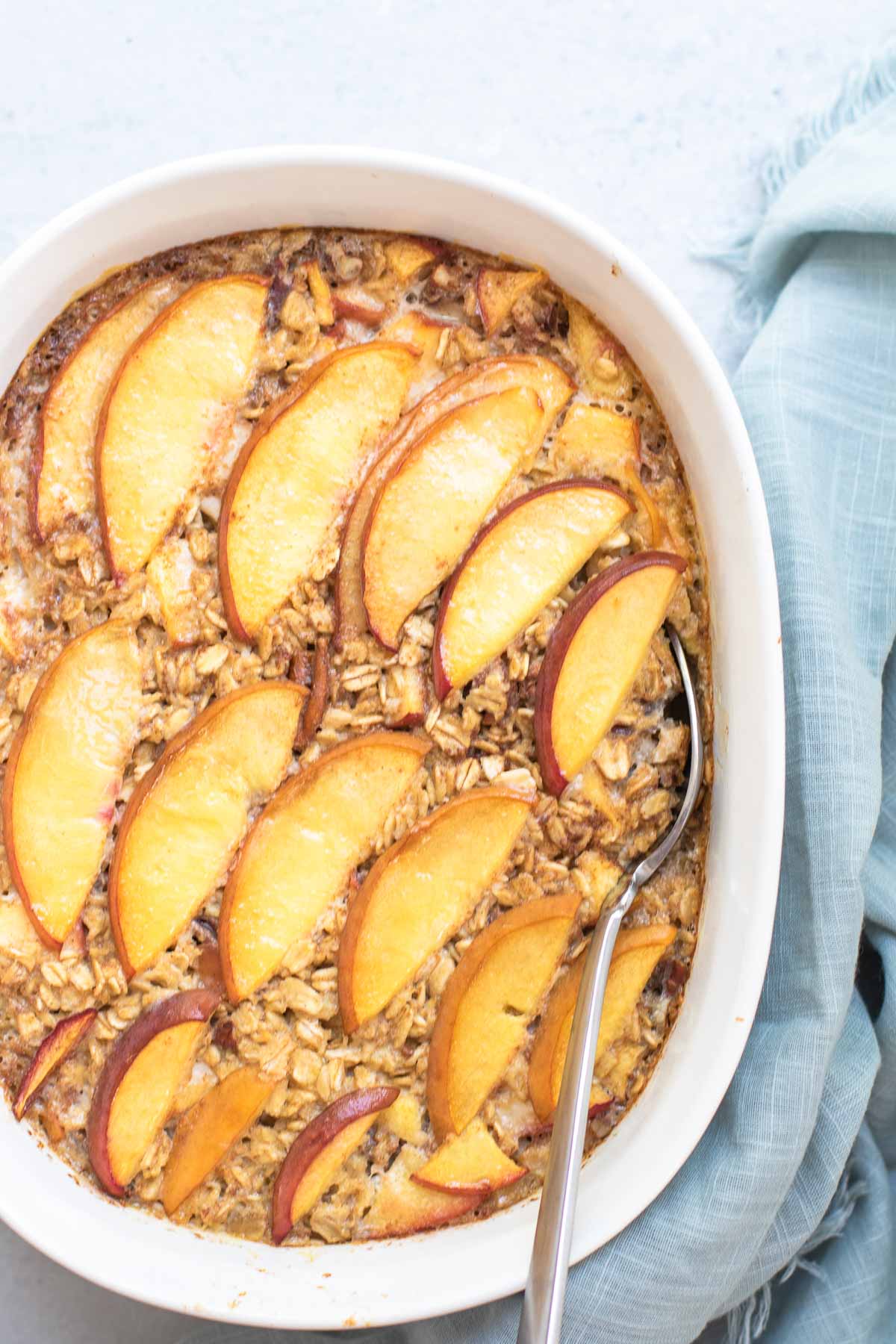 Peach Baked Oatmeal in a white casserole dish with a blue napkin around it.