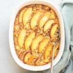 Peach topped baked oats in a white casserole dish with a spoon inserted.