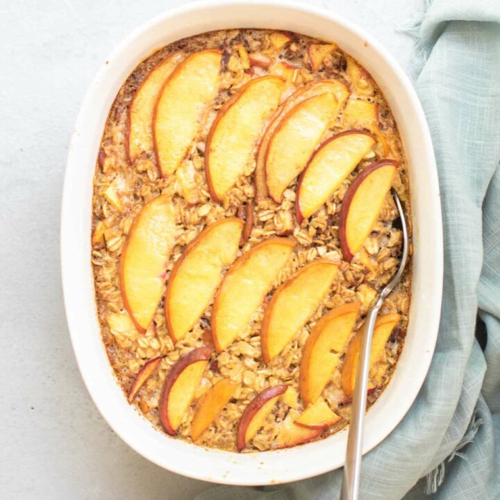 Peach topped baked oats in a white casserole dish with a spoon inserted.