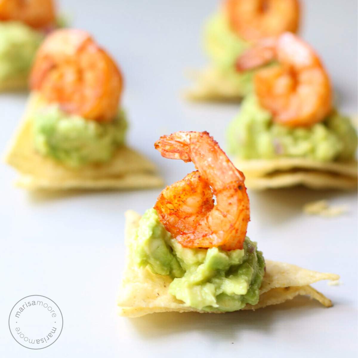 Tortilla Chips each topped with guacamole and a shrimp.