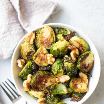 Roasted Brussels Sprouts in a white bowl with a gray napkin and two forks