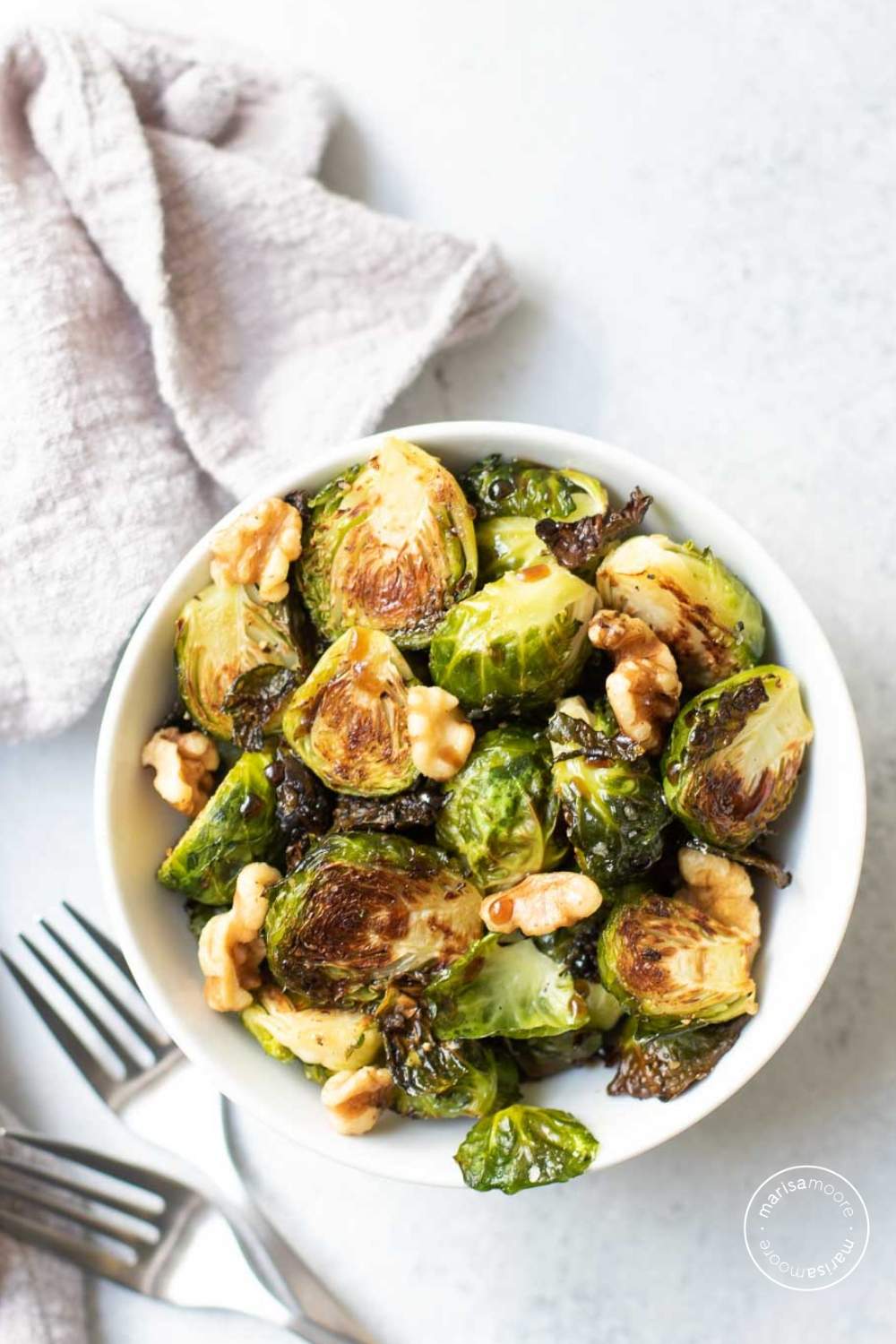 Roasted Brussels Sprouts in a white bowl with a gray napkin and two forks