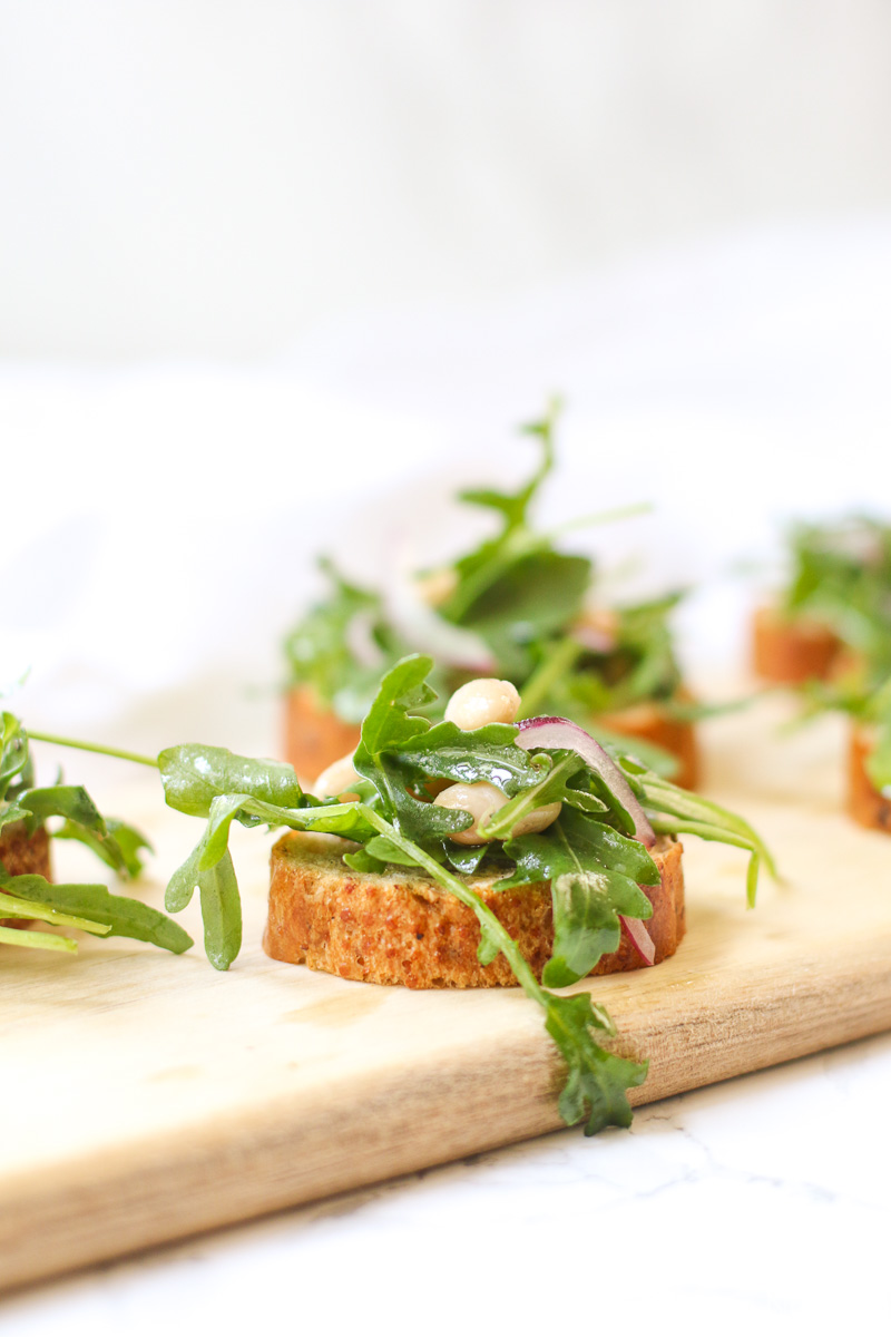 White Bean Arugula Crostini on slim wooden cutting board