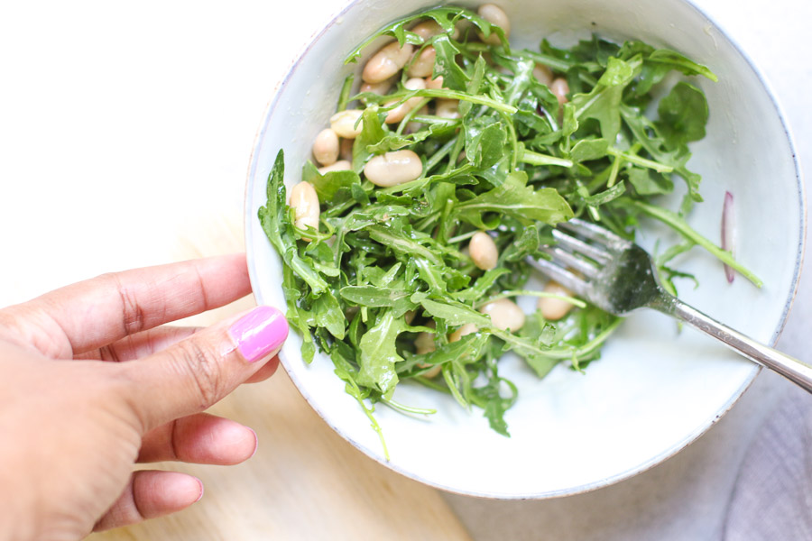 White Bean Arugula in Salad bowl with hand showing it off