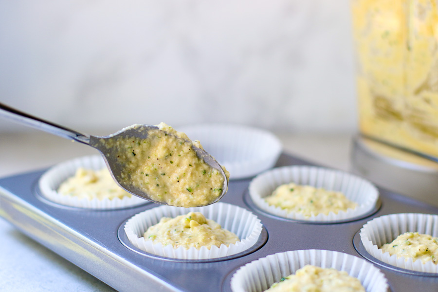 Adding zucchini muffin batter into tin with a spoon