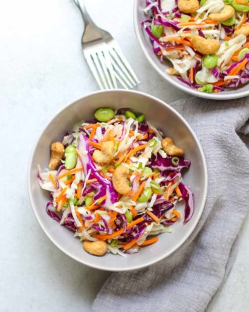 Cashew Cabbage Salad in two serving bowls with two forks and a gray napkin