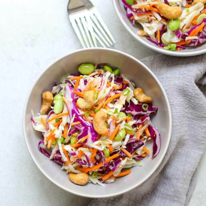 Cashew Cabbage Salad in two serving bowls with two forks and a gray napkin