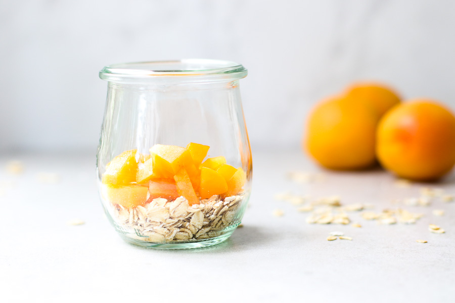 Oats topped with apricots in a jar with apricots in the background