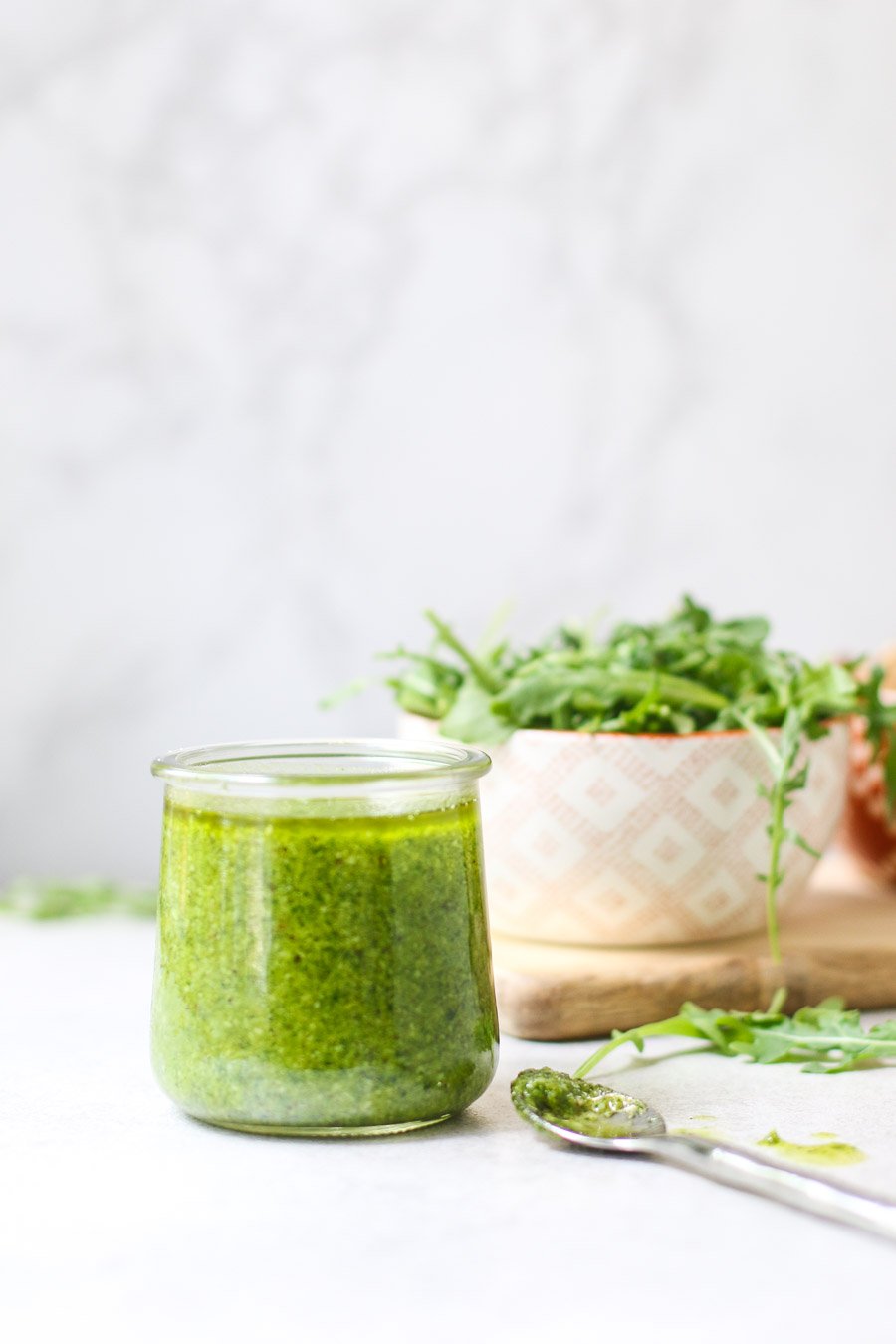 Arugula Walnut Pesto in jar with arugula in a bowl in the backdrop