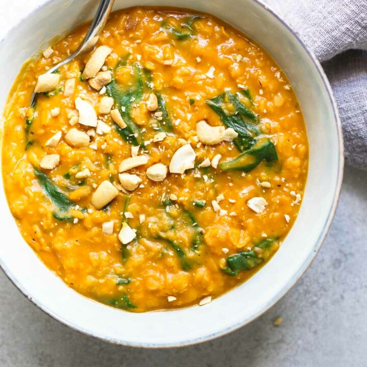 Pumpkin Lentil Curry in a bowl with cashews in a gray bowl with gray napkin