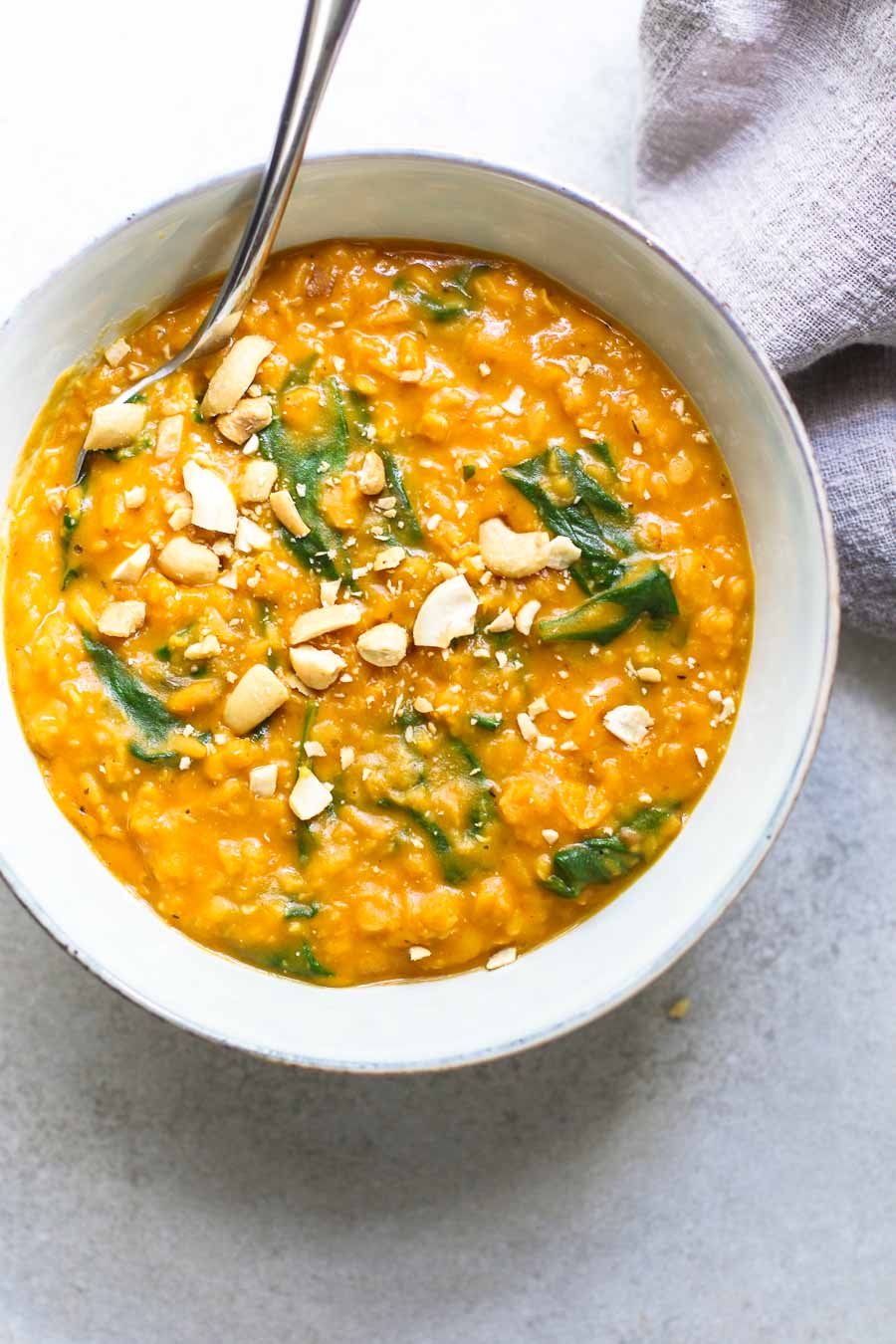 Pumpkin Lentil Curry in a bowl with cashews in a gray bowl with gray napkin