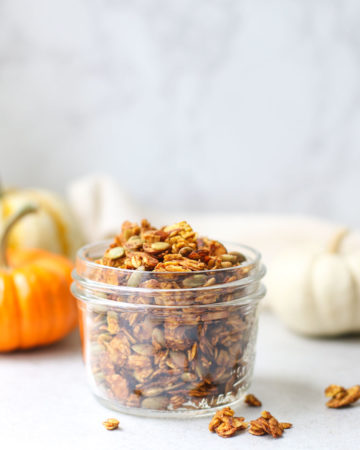 Pumpkin spice granola in small mason jar with mini colored pumpkins in the background