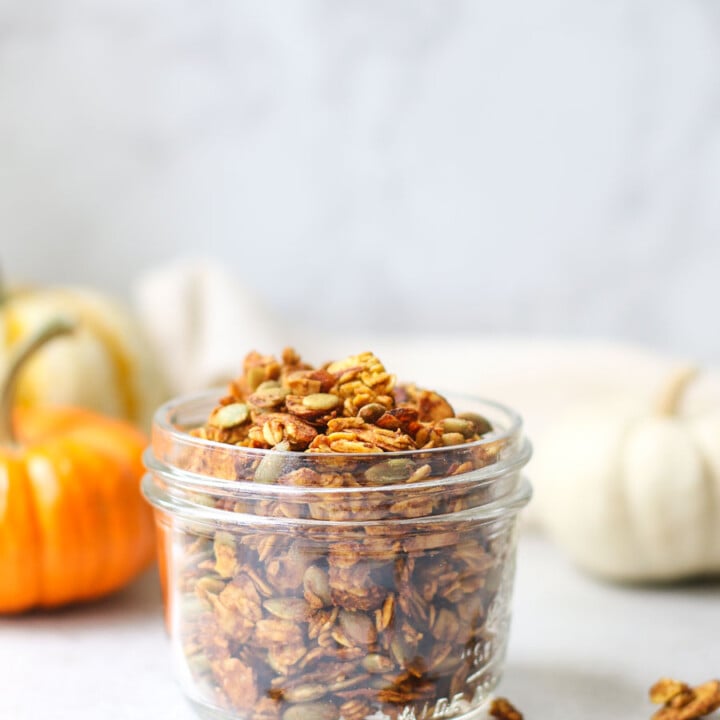 Pumpkin spice granola in small mason jar with mini colored pumpkins in the background