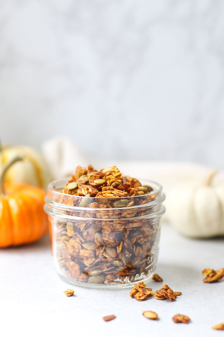 Pumpkin spice granola in small mason jar with mini colored pumpkins in the background