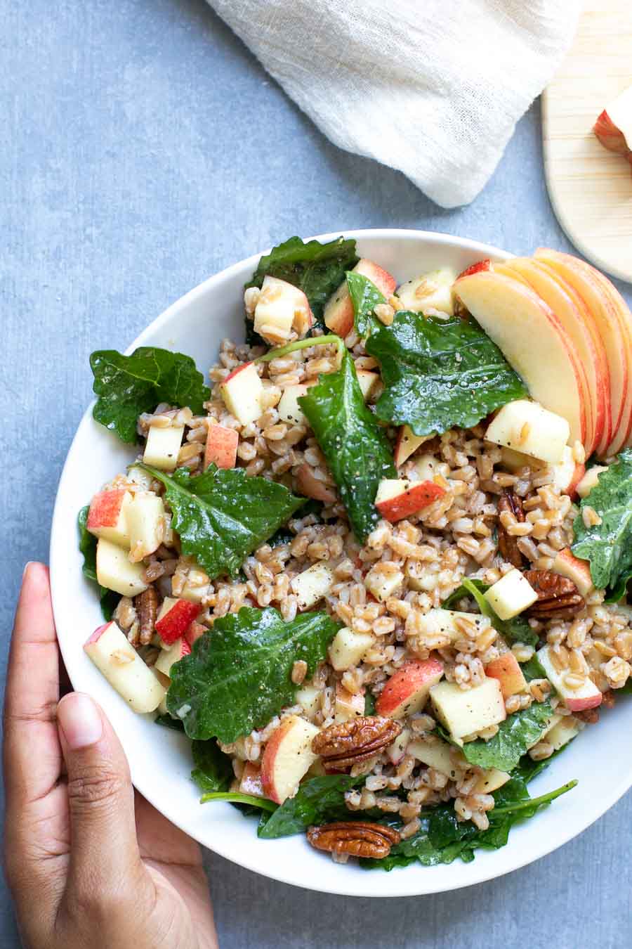 Apple Pecan Farro Salad in bowl with hand on side