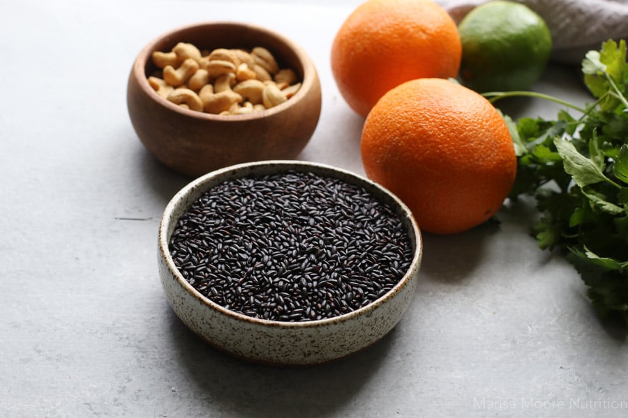 black rice and cashews in bowls with whole oranges in the background