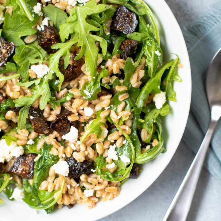 Fig Farro Arugula Salad in white bowl with blue napkin and utensils