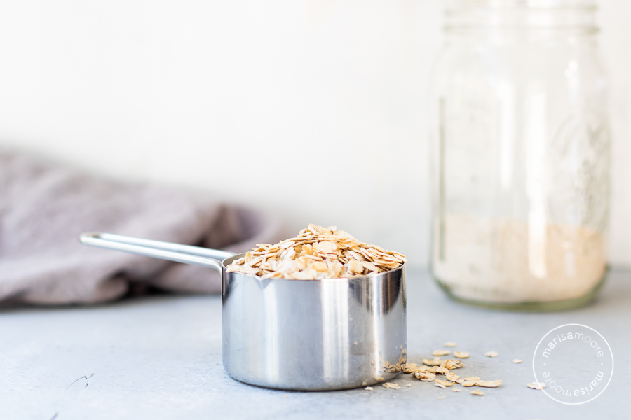 Oats in a measuring cup with oat flour in background