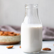 Pecan milk in a bottle with pecans in the background