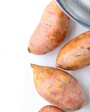 Whole sweet potatoes on a white background with colander