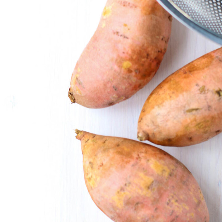 Whole sweet potatoes on a white background with colander
