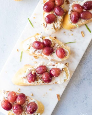 Roasted Grape Goat Cheese Toasts on a white cheese board