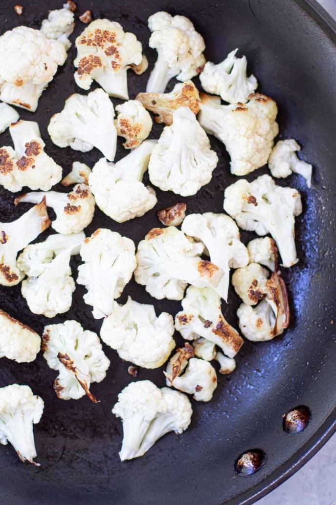 cauliflower sautéed a black skillet with a wooden spatula