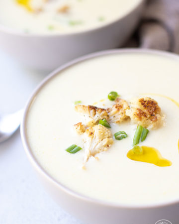 Cauliflower soup in two gray bowls with a spoon and napkin