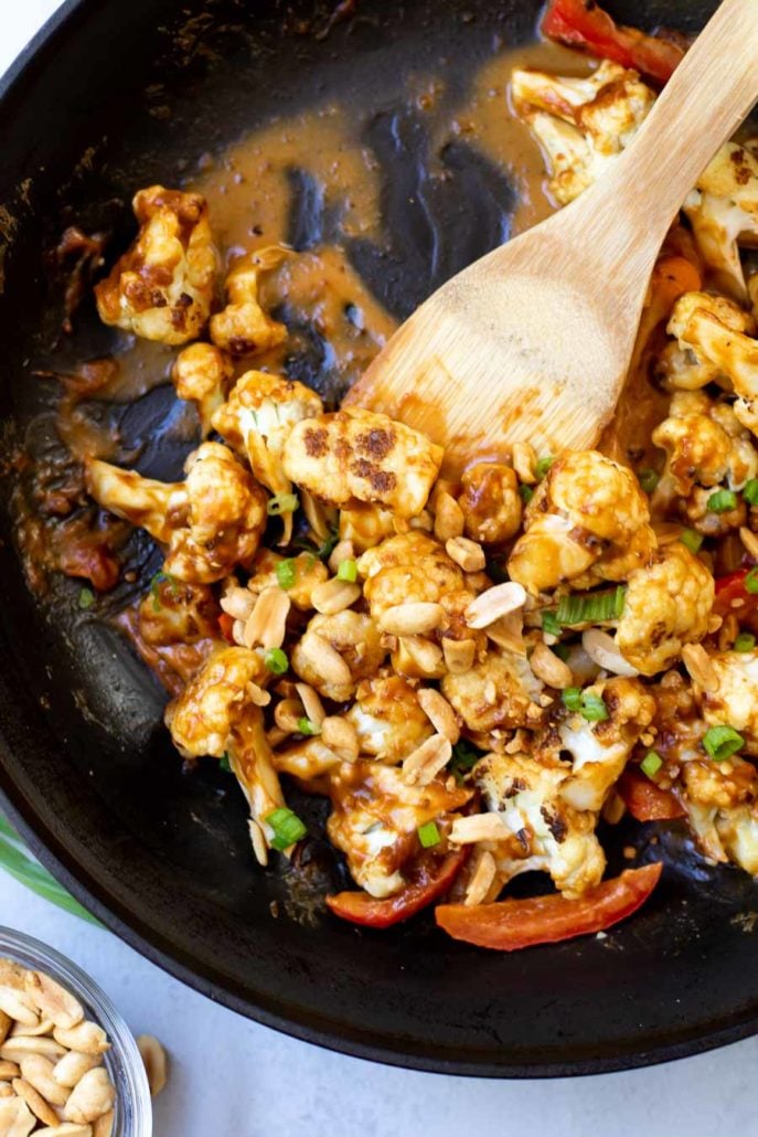 cauliflower stir-fry in a black skillet with a wooden spatula