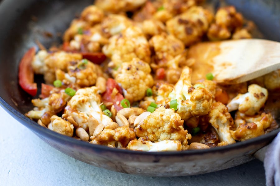 cauliflower stir-fry in a black skillet with a wooden spatula