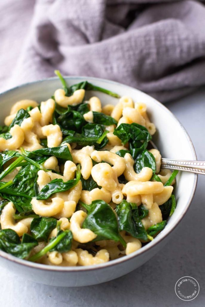 Bowl of spinach mac and cheese with gray napkin in the background