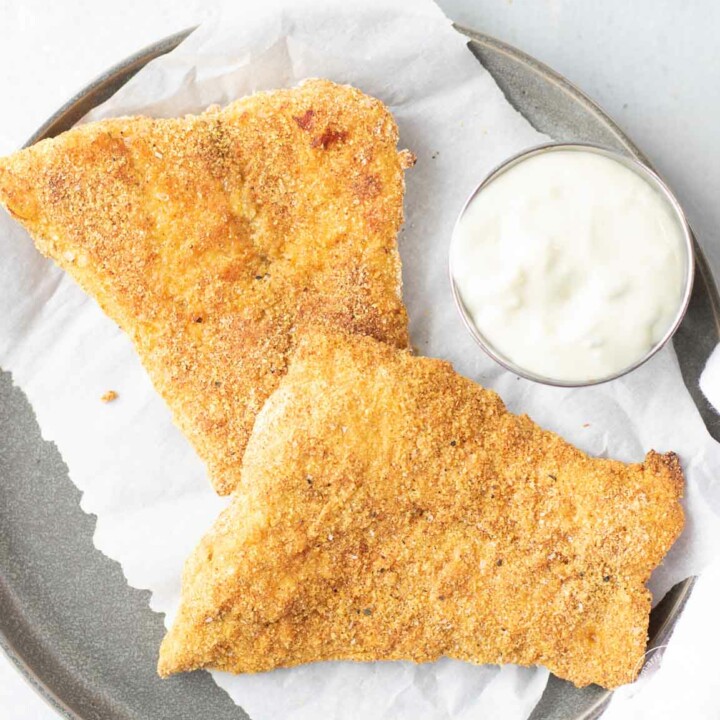 two pieces of air fryer fish on a blue plate with parchment