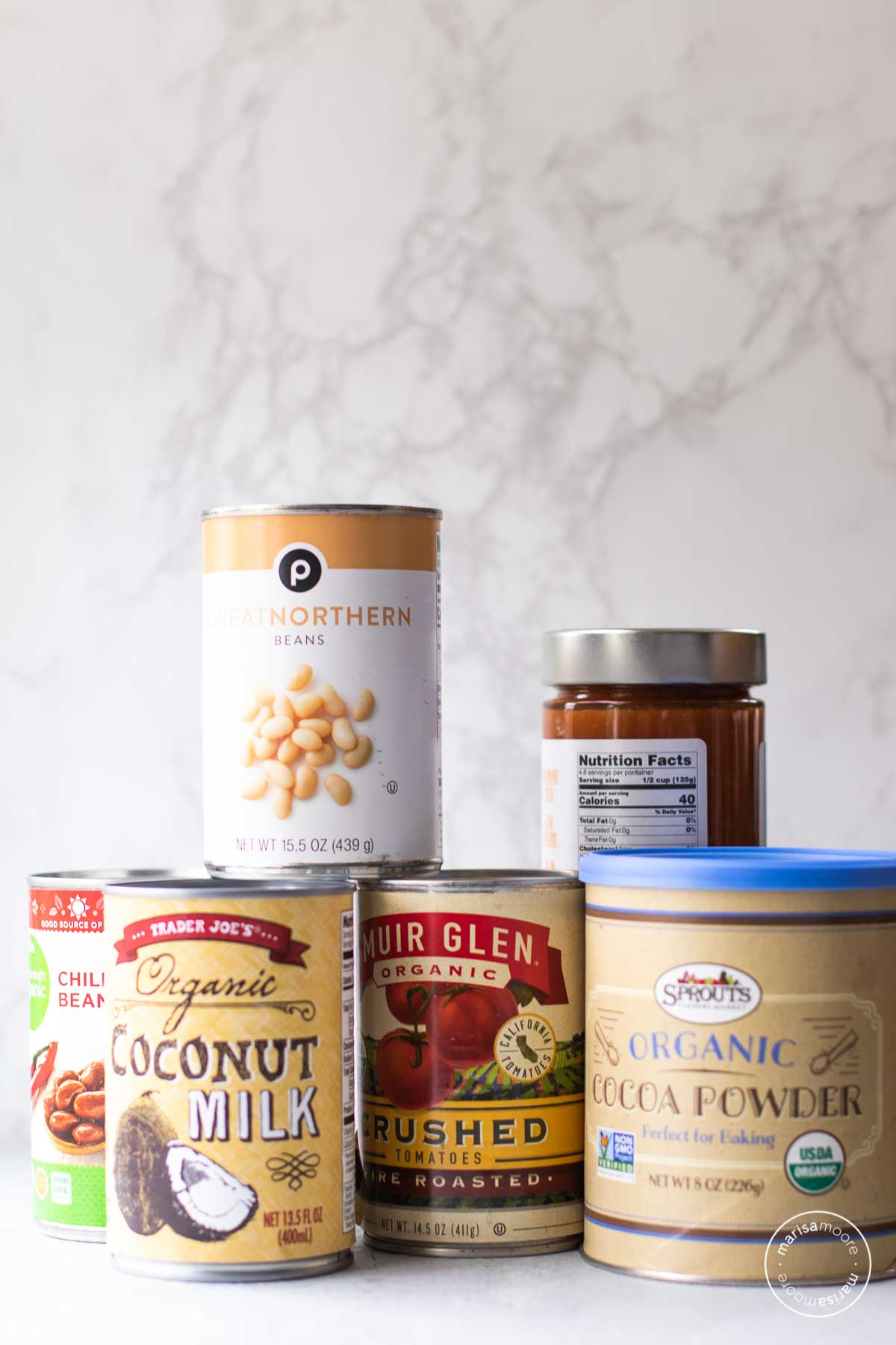 Cans of white beans, chili beans, tomatoes and coconut milk stacked. 