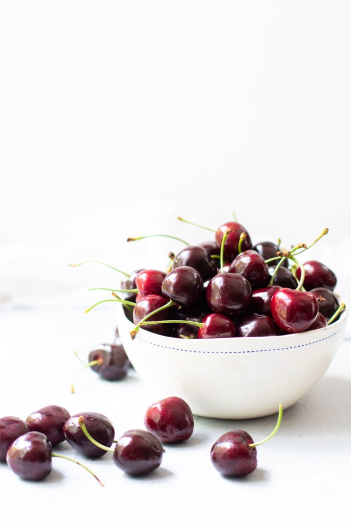 cherries in a white bowl and scattered around the bowl