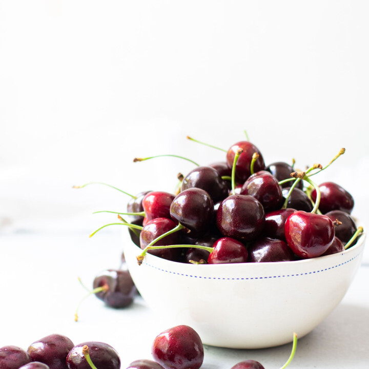 cherries in a white bowl and scattered around the bowl