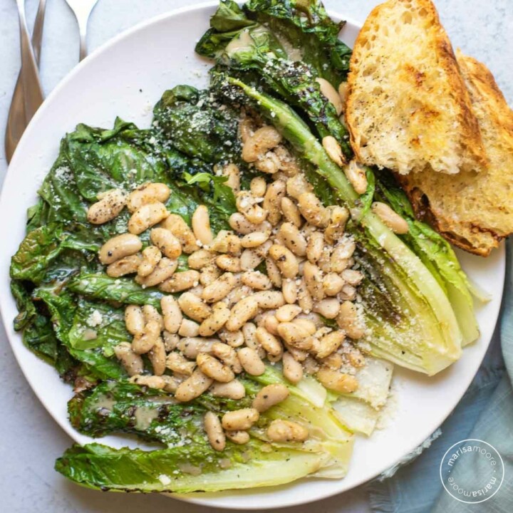 Grilled romaine topped with white beans and grilled bread on white plate