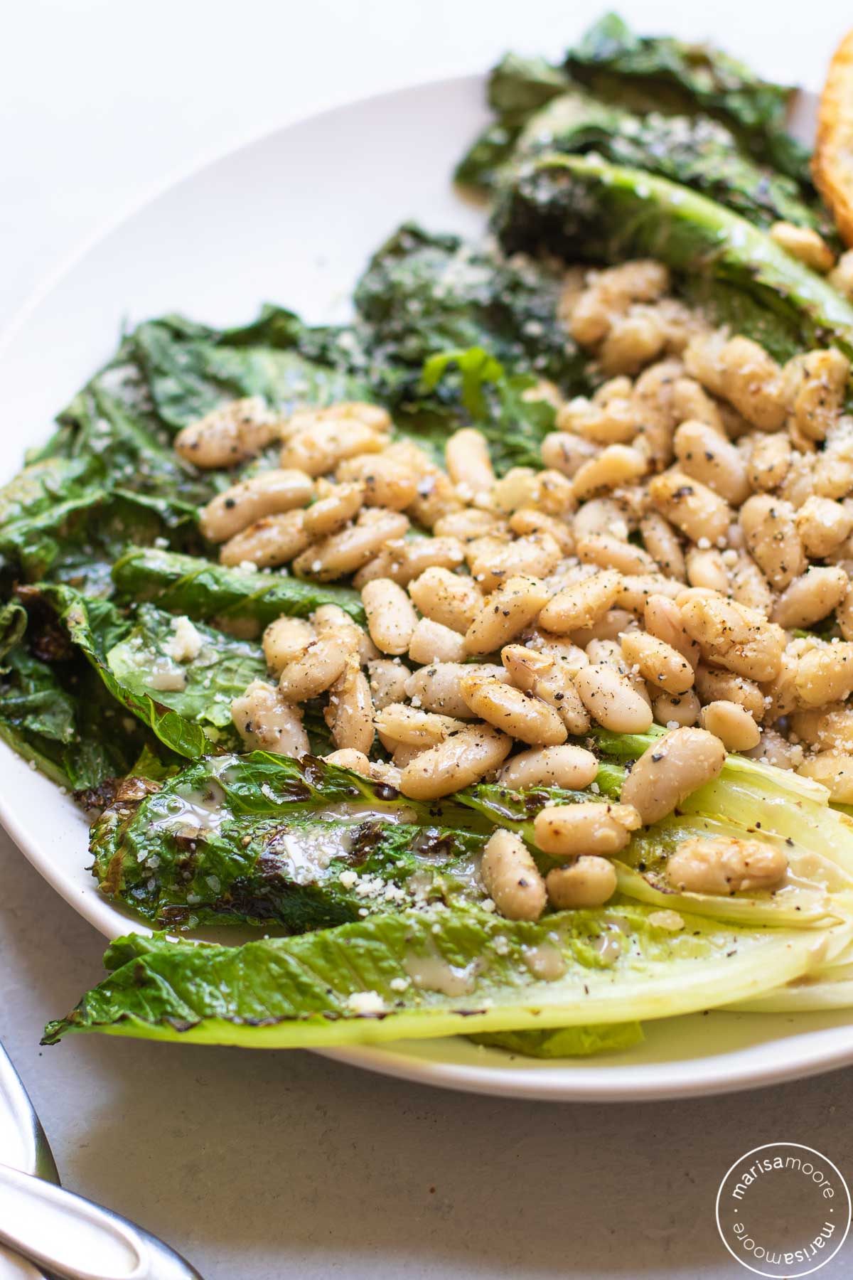 Whole leaves grilled lettuce with white beans on top on a white plate