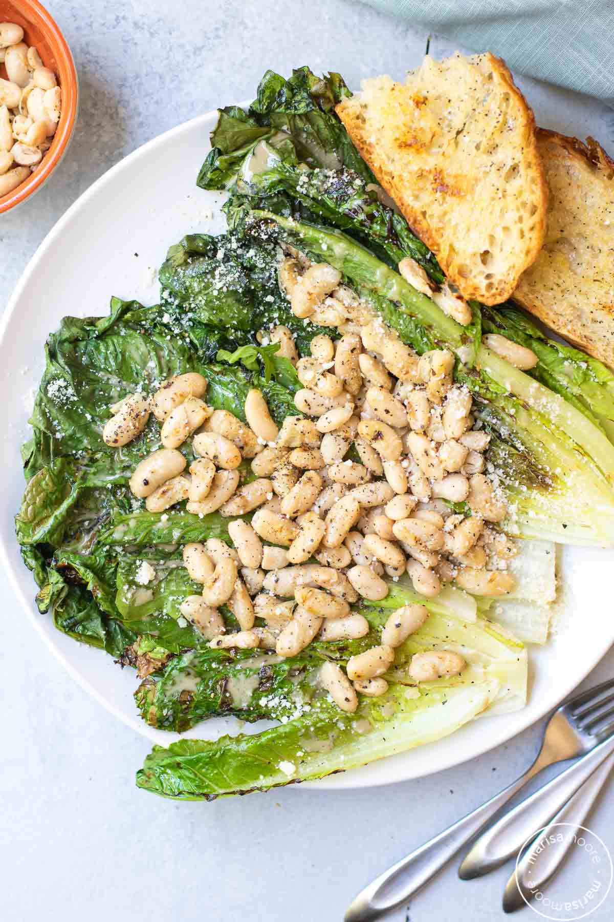 White Bean Salad over grilled lettuce with crusty grilled bread on a white plate