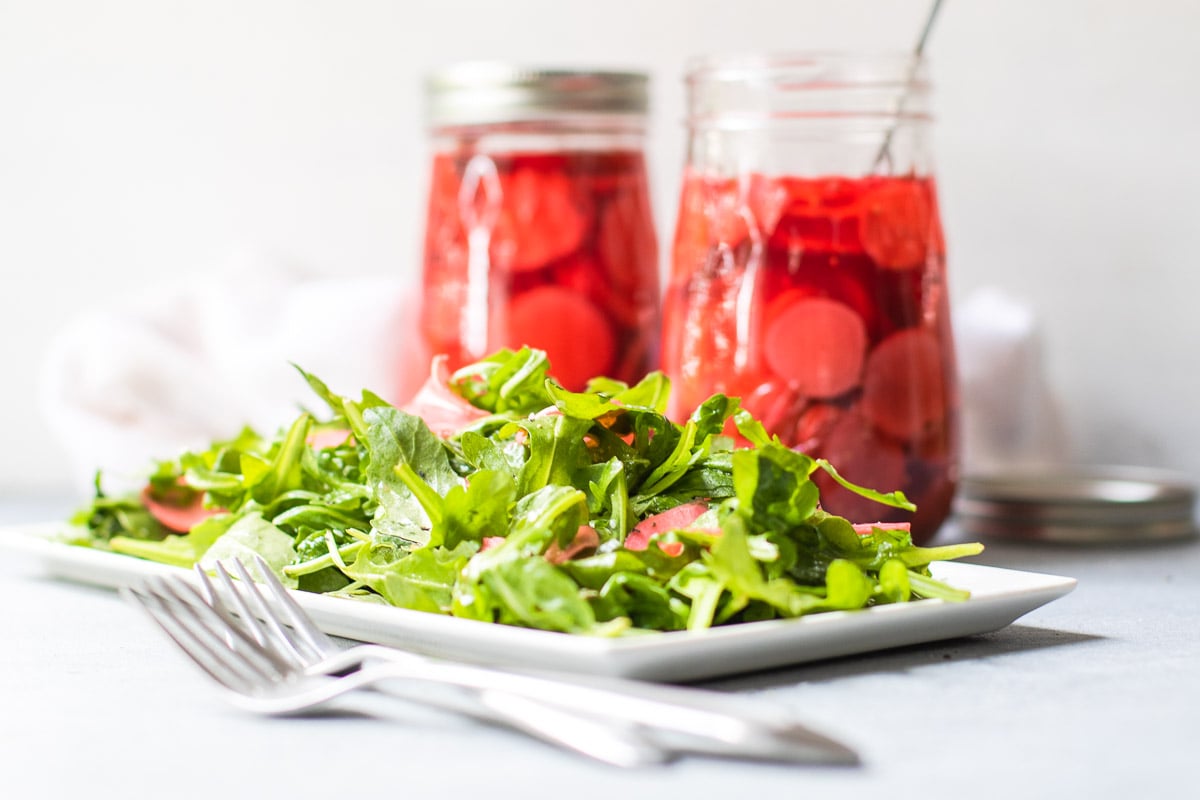 Green salad with two jars of quick pickles and two forks