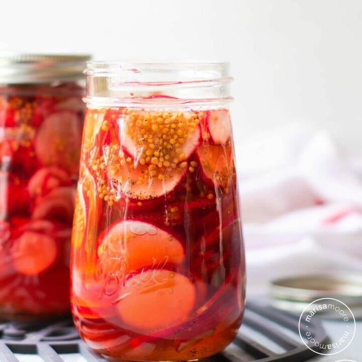 radishes in pickling brine in jars with a white towel in background