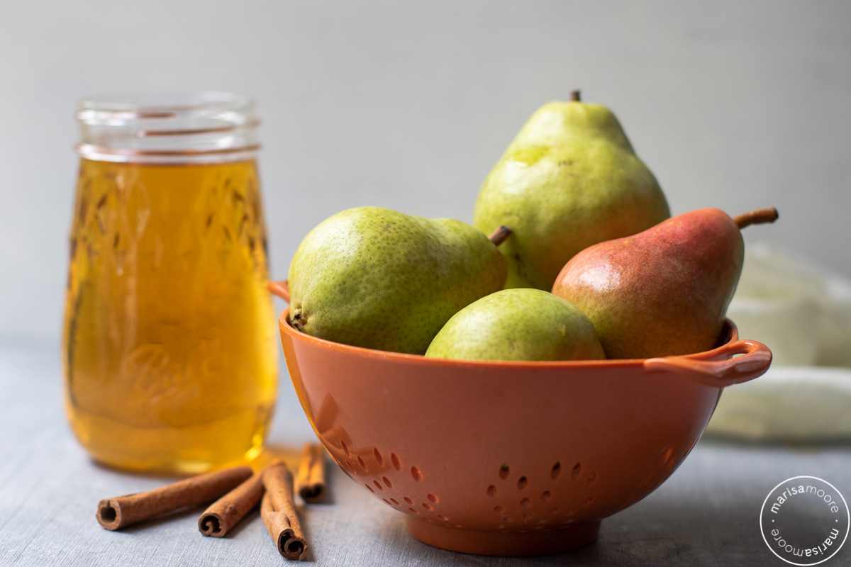 orange colander of fresh pears, with cinnamon sticks, and apple juice in a jar