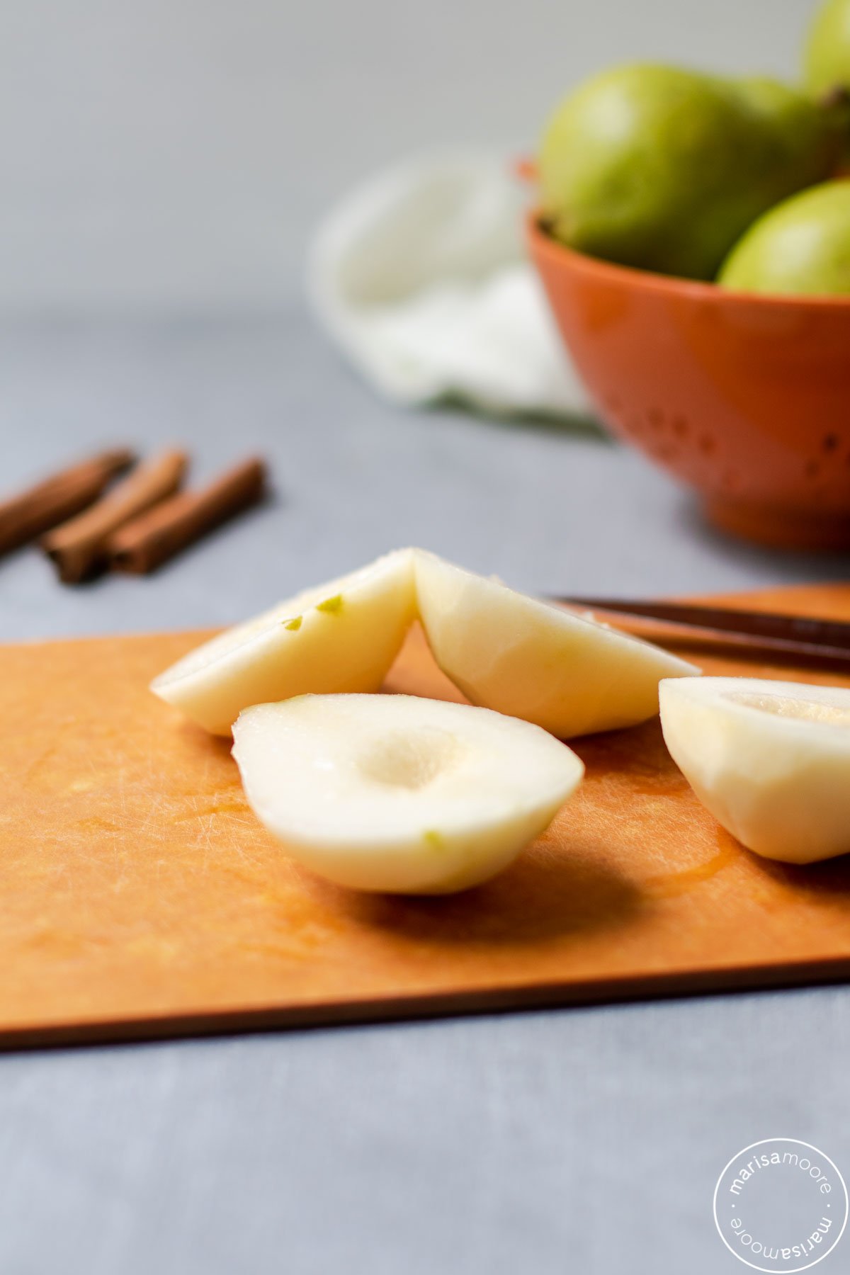 peeled, halved, and scooped pears on a cutting board with whole pears in background