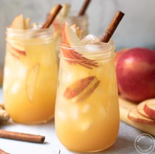 two fluted jars with the apple mocktail inside garnished with cinnamon sticks and apple slices