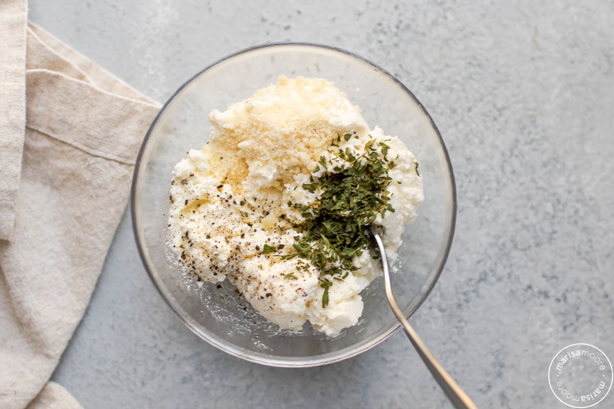 Ricotta cheese with parsley and parmesan in a small glass bowl with a spoon 